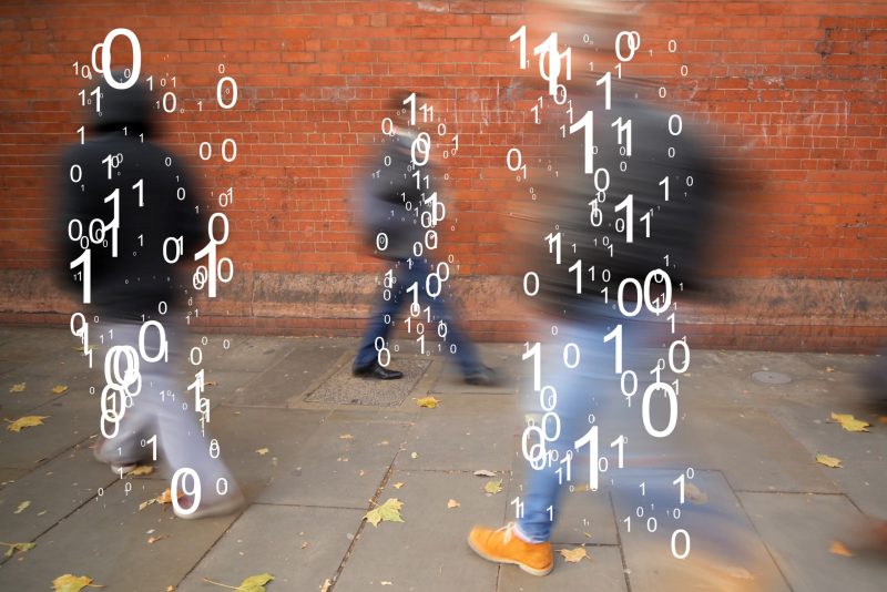 The binary code is superimposed over figures walking along a sidewalk