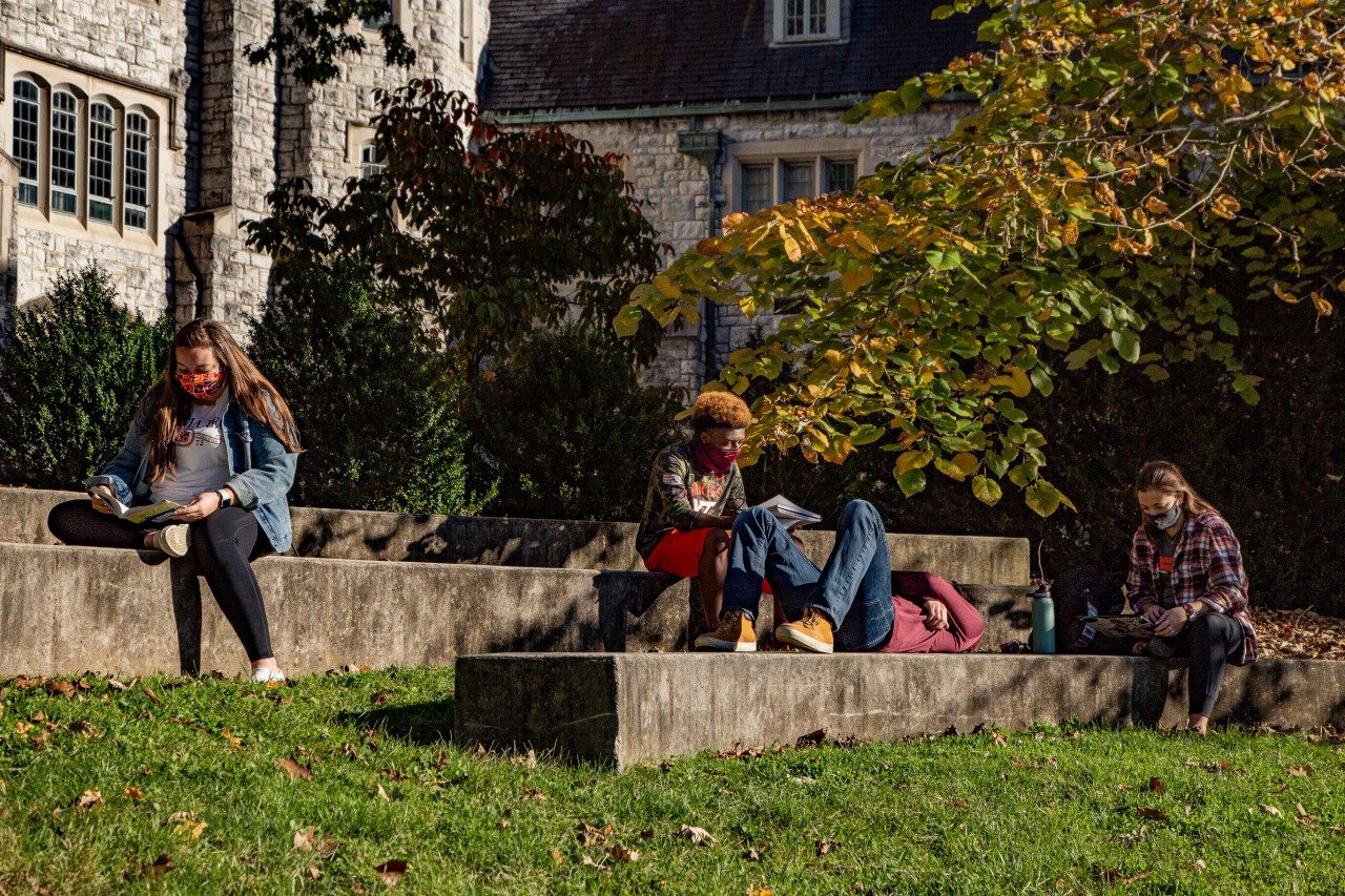 four young adult students sit on the steps in the ag quad, focused on their  books in their laps. Two are white women, one is a black man, and the fourth is a white man. They all wear hokie colored face masks.