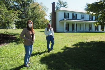 The two women, who are the 2020 McCombs scholars, stand in front of Solitude, a historic house. Both wear masks.
