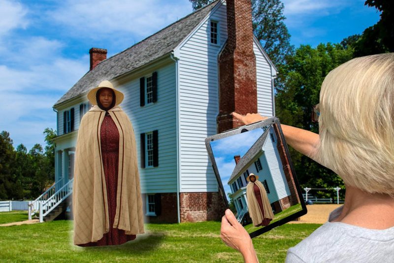 A woman looks at a digital tablet and sees a Civil War era woman standing in front of a historic house.