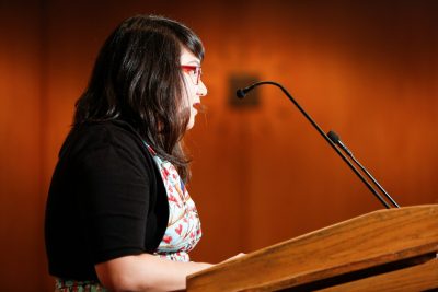 A profile view: Janine Joseph speaks at a lectern. 