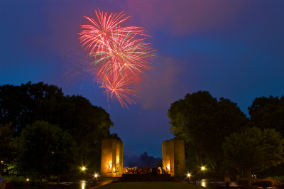 Fireworks are pictured above the Pylons and the Drillfield at Virginia Tech. Several students are standing around the Pylons to watch the fireworks.