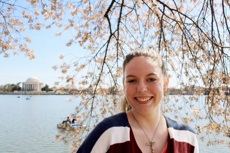 In D.C., Megan wears a striped shirt and stands in front of a cherry blossom tree with the Jefferson Monument and Patuxent River in the background.