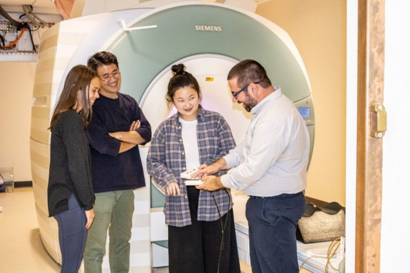 Students and professors stand in front of the functional magnetic resonance imaging scanner 
