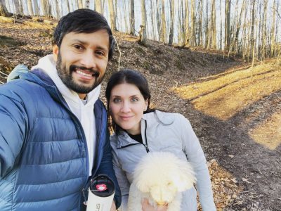(From left) Vinodh Venkatesh and María del Carmen Caña Jiménez, smiling, pose for a photo in the woods with a dog.