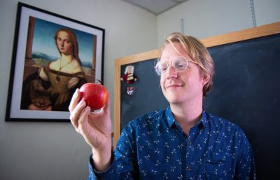 Dan Hoek holding an apple in front of a chalkboard