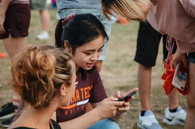 Students gather around together to look at a cellphone screen
