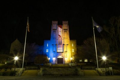 Photo of Burruss Hall illuminated in blue and yellow