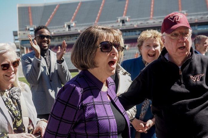 Rosemary Goss (center) and her husband, Bob, look astonished as they realize that the gateway the Virginia Tech football team uses to enter Lane Stadium had been named in her honor. André Davis, a property management alumnus and retired National Football League wide receiver and kick returner, applauds in the background, while advisory board member Alice Fletcher (left) watches and a beaming Julia Beamish (standing behind Bob Goss), head of the Department of Apparel, Housing, and Resource Management, delights in her colleague’s response.