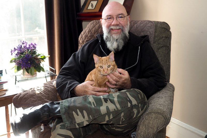 Jeff Mann sits in his writing space with his orange tabby cat, Rory, on his lap.