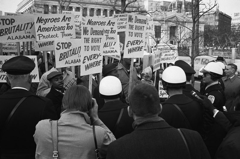African American demonstrators outside the White House March 12, 1965 with signs reading, "We demand the right to vote, everywhere" and protesting police brutality against civil rights demonstrators in Selma, Alabama.