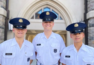 Cadets in white uniform shirts stand smiling outside the archway at Upper Quad Hall North.