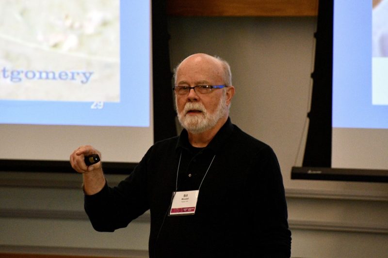 Man stands at front of auditorium during presentation.