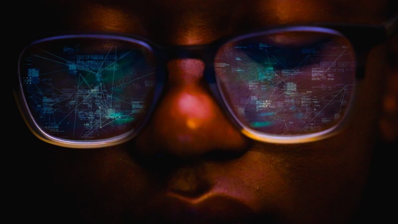 close up shot of a person and a reflection of a computer screen in their glasses.