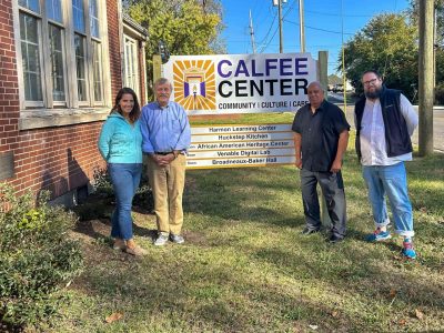 Three men and a woman stand side by side, smiling, in front of  the Calfee Cultural and Community Center sign.