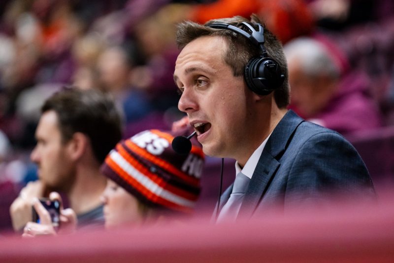 Male sports broadcaster wearing a headset in crowded coliseum.