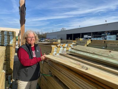 Women picks up lumber outside hardware store.