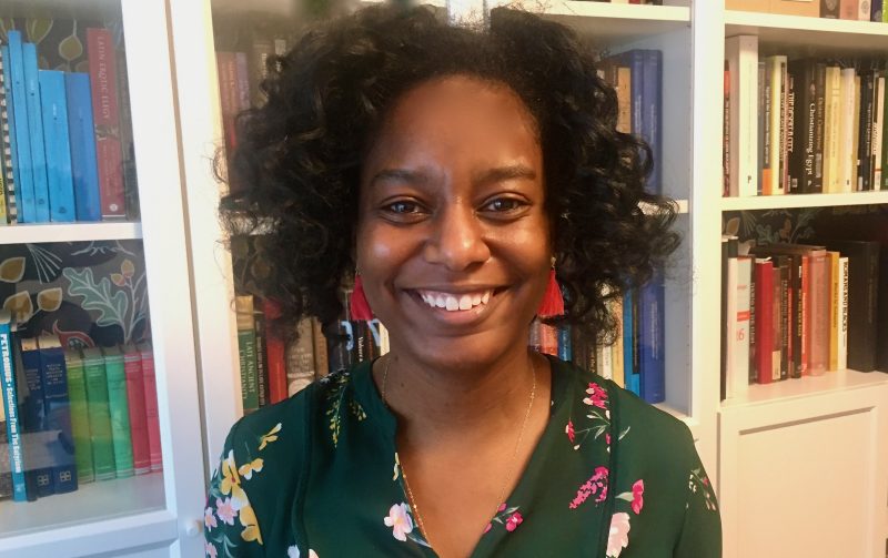 Candace Buckner, Assistant Professor, stands in front of a bookshelf in a portrait photo