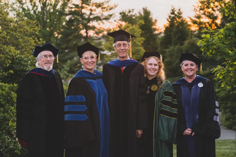 male student graduating with his Ph.D. with a group of his professors