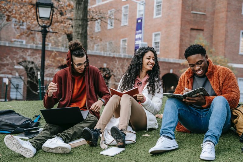 a racially mixed group of college students laugh as they study together in an outside setting