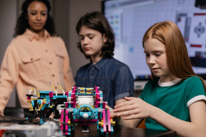 two students, under the supervision of their teacher, work on small robots