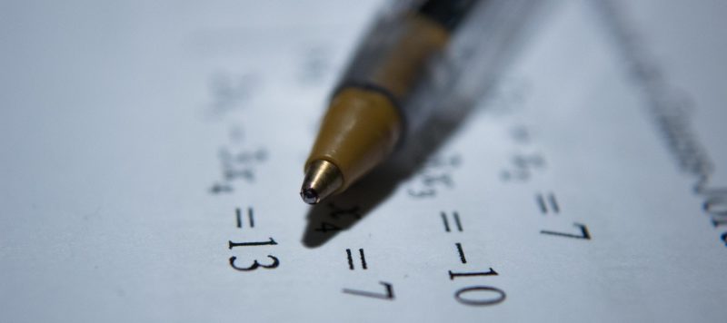 a ballpoint pen sits atop a quiz paper with algebraic equations