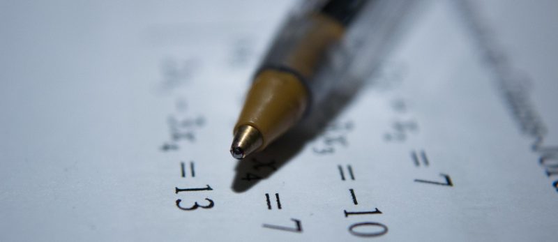a ballpoint pen sits atop a quiz paper with algebraic equations