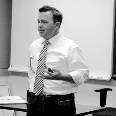 dr. david kniola is a white man. in this black and white picture, he is lecturing at the front of a classroom