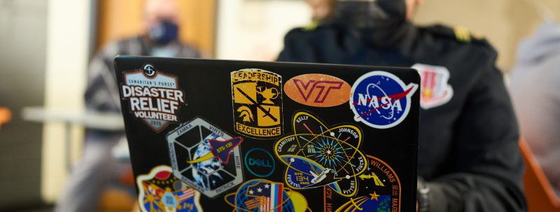 a student works on their laptop. its cover has many stem related stickers affixed to it