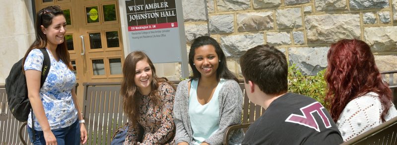 a group of students chat in front of a building on campus drive