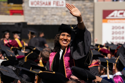 a doctoral graduate waves happily from the crowd