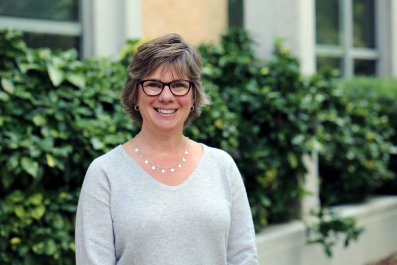 Dr. Kristin Gehsmann, Director of the School of Education, smiles confidently at the camera, wearing glasses and  grey sweater