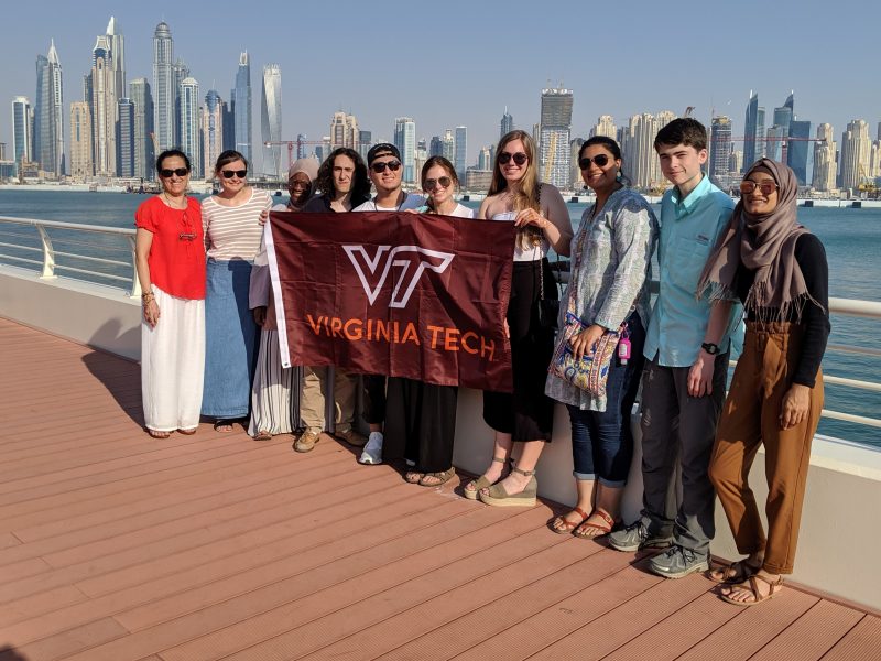 A group of students took a moment to express their Hokie pride in Dubai, holding a Virginia Tech banner with the city's tall buildings in the background. 
