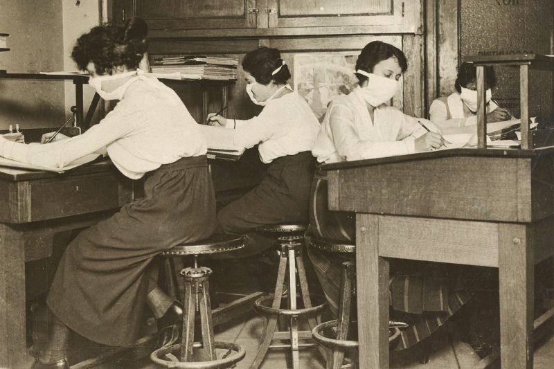 Clerks in masks collect and classify statistics during the 1918 influenza pandemic. Courtesy of the National Archives.