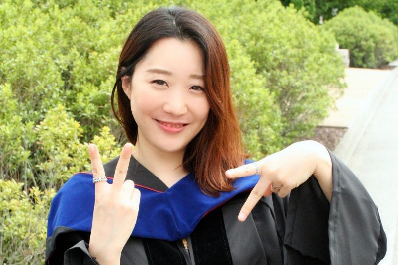 Eunkyung “Lucy” Shin, wearing her graduation gown, uses her fingers to spell out "VT"