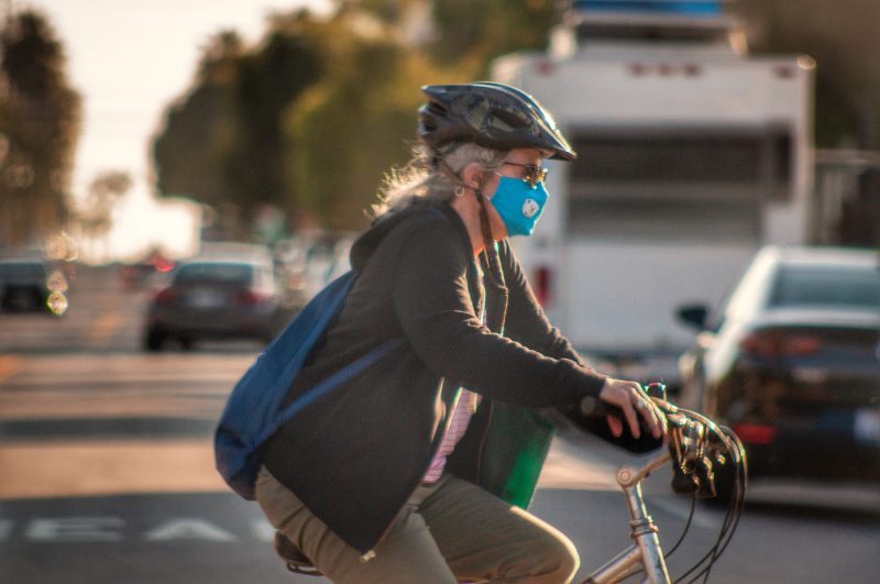 Photo of a woman biking across a street while wearing a mask amid the COVID-19 pandemic.
