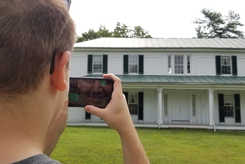 A student working with the VT 150: Visualizing Virginia Tech History project in 2019 views Virginia Tech’s oldest building, Solitude, through a smartphone.