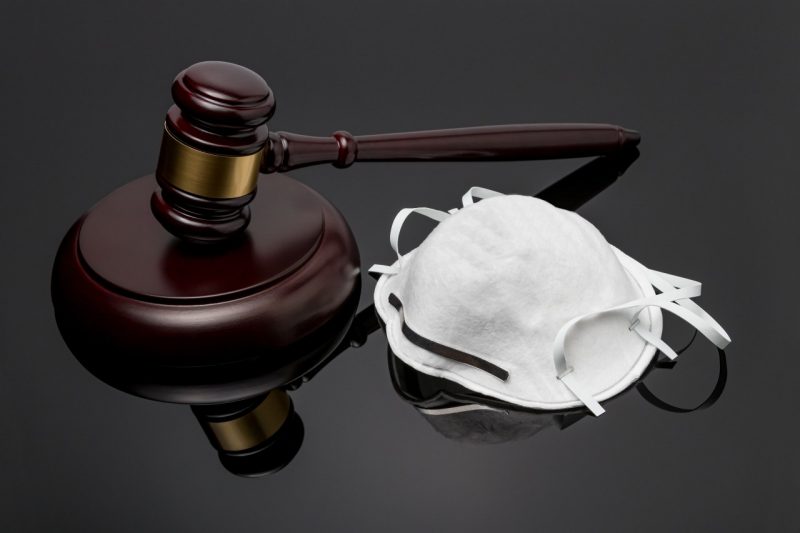 N95 face mask and gavel on black background. Concept of face covering mandate, ordinance, lawsuit, freedom, constitutional rights during Covid-19 coronavirus pandemic