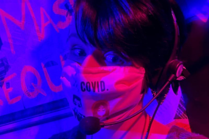 Casey Duke wears a mask. She is lit with purple and fuchsia lights. 