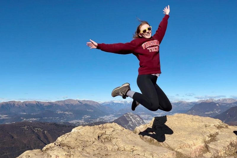 A student in a Virginia Tech sweatshirt jumping on a mountaintop
