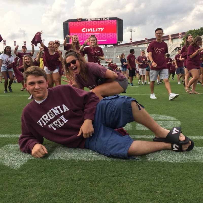 Jackson Ribler lays on the field in Lane Stadium and poses for a photo while surrounded by many other excited Virginia Tech students.