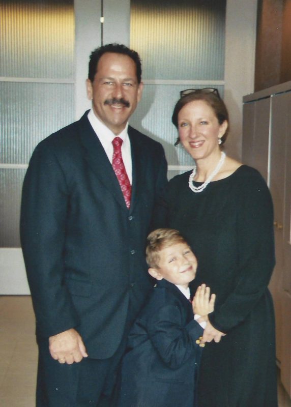 Larry and Rebecca Ribler pose for a photo with their son, Jackson, who was a child at the time. All three are wearing formal attire.