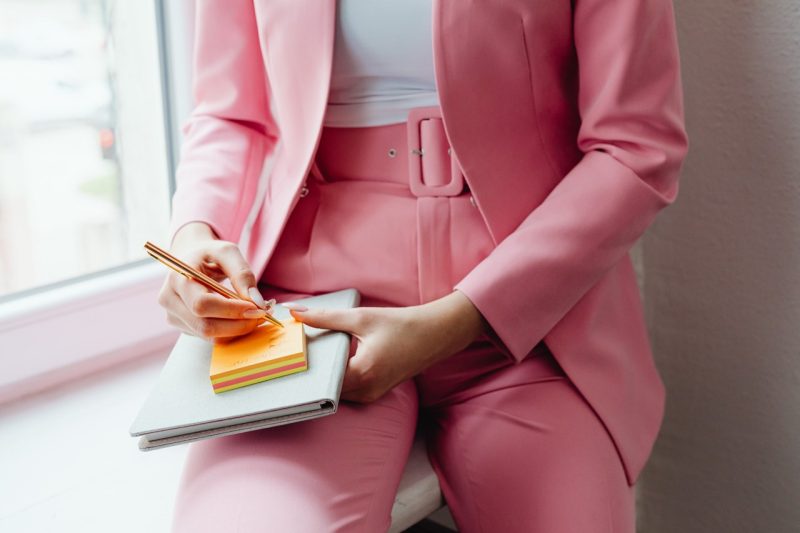 Person wearing a pink writes notes in a notebook.