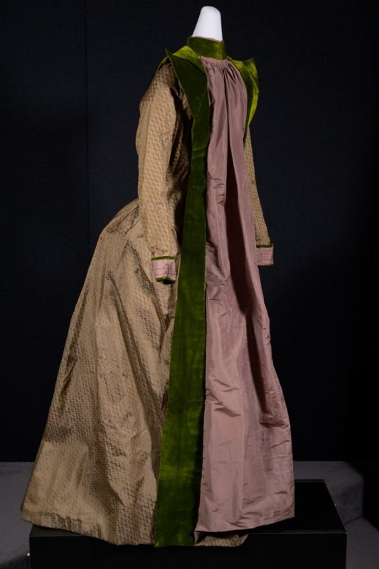 A 19th-century house dress made of muted pink and brown fabric with a pointed olive green collar and a brocade pattern resembling scales.