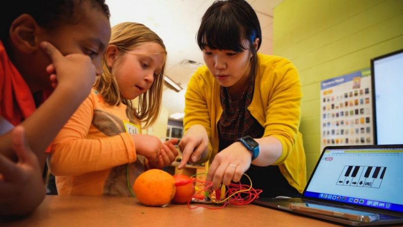Koeun Choi shows students how to connect oranges and a tomato to a computer program that makes different sounds. 