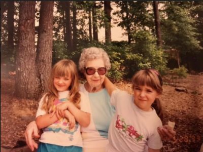 a grandmother and her two granddaughters pose in front of a wooded scene
