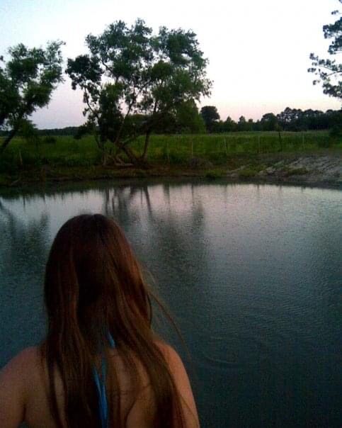 we look over a young teen girl's shoulder at a retaining pond in a rural farm setting