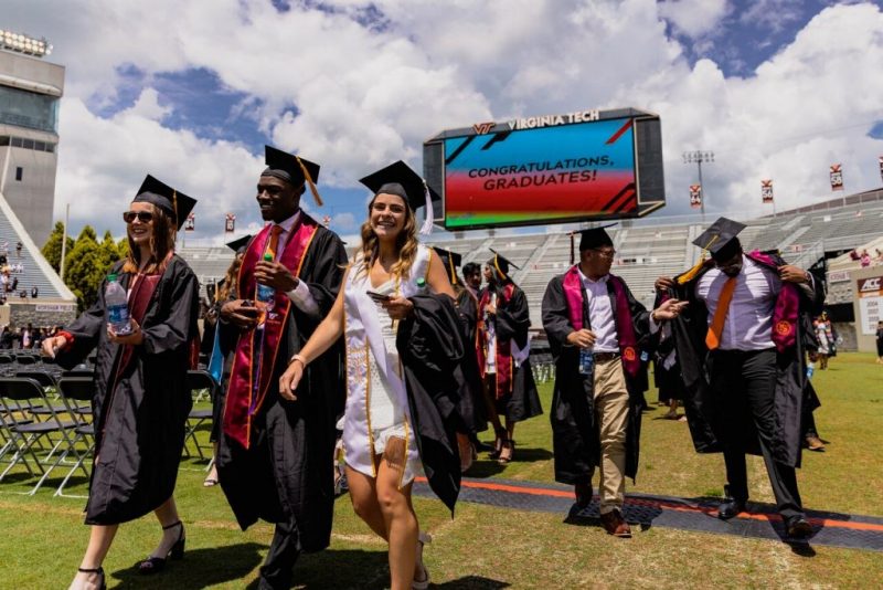 Students are shown walking along Lane Stadium field during commencement