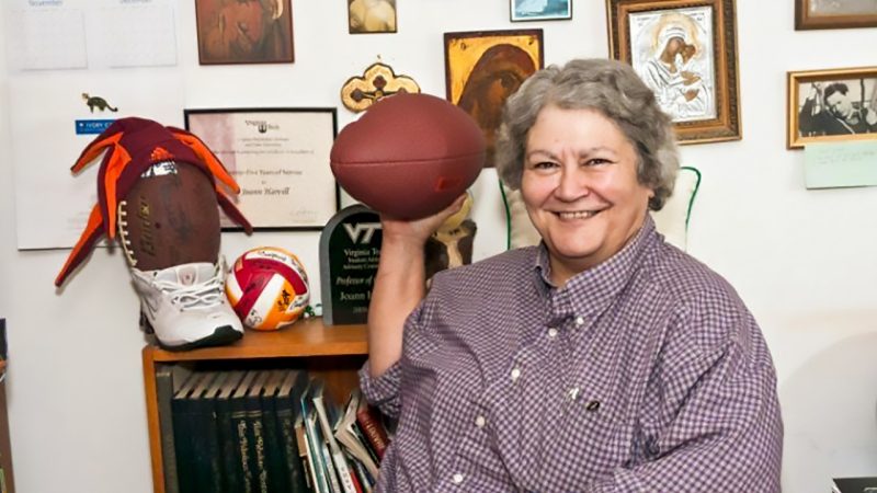 JoAnn wears a maroon checked shirt and holds a football. 