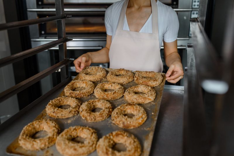 A baker holds a tray with fresh bagels
